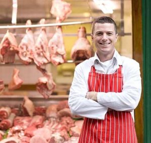 Butcher standing in front of butcher shop window